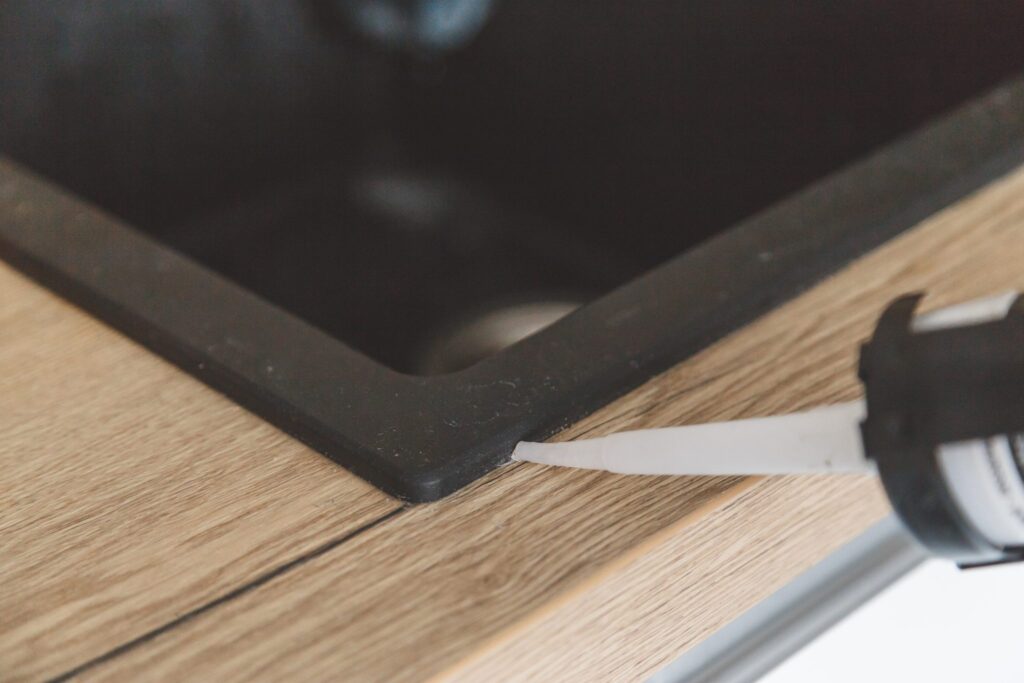 3 Things to Remember When It Comes to Home Caulking 8 Man sealing kitchen sink joint between sink and countertop by silicone sealant